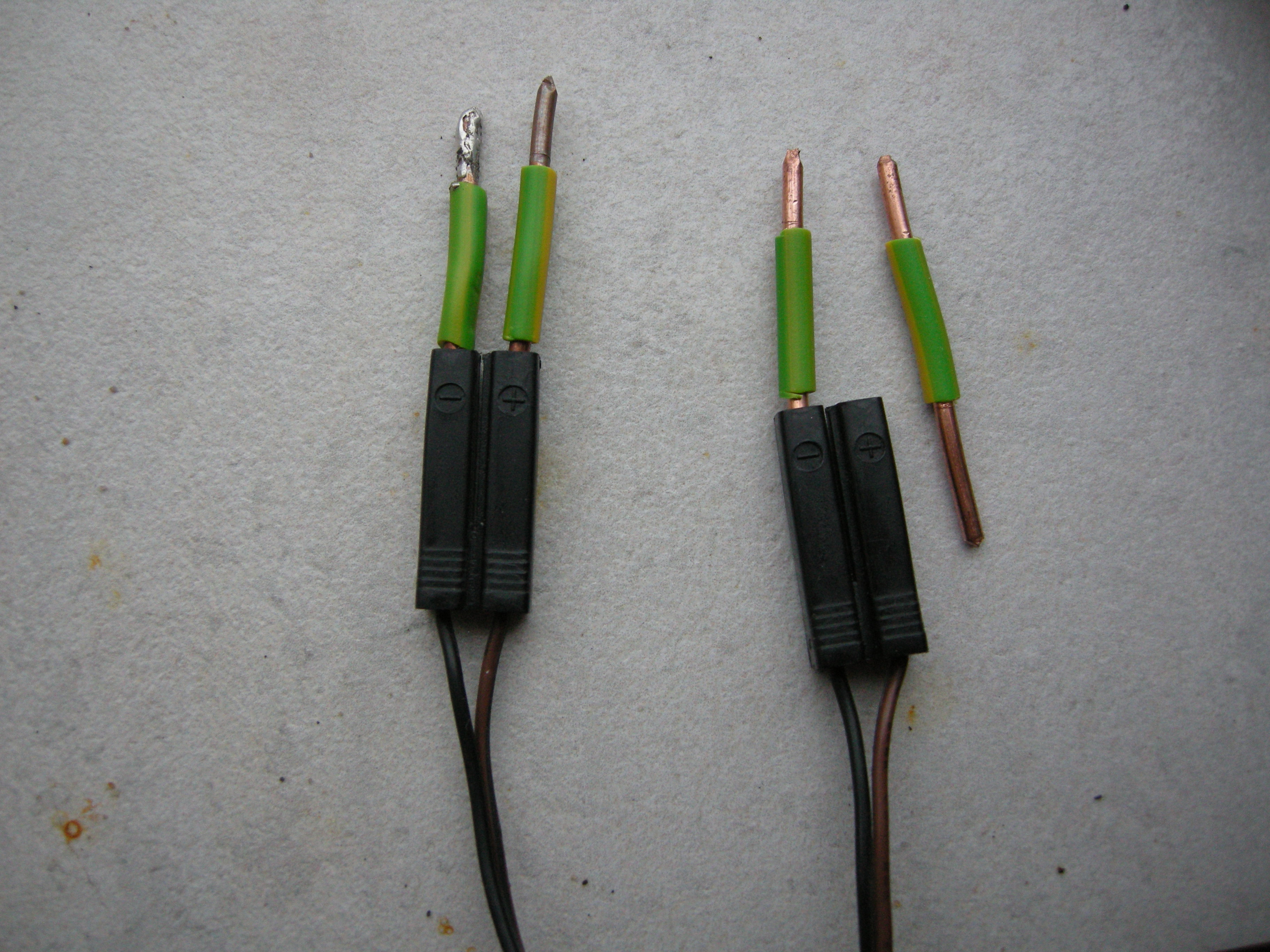 Two speaker connectors made of black plastic, three out of the four holes plugged by wire, one wire inside tinned